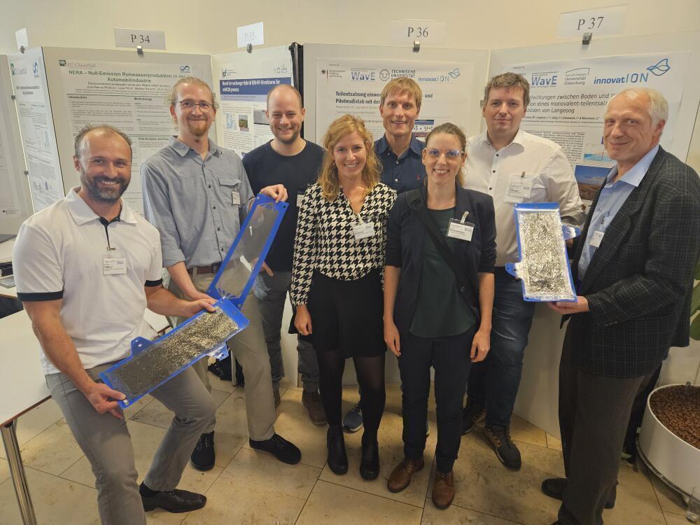 Project partner in front of poster from innovatION, holding an electrochemical cell